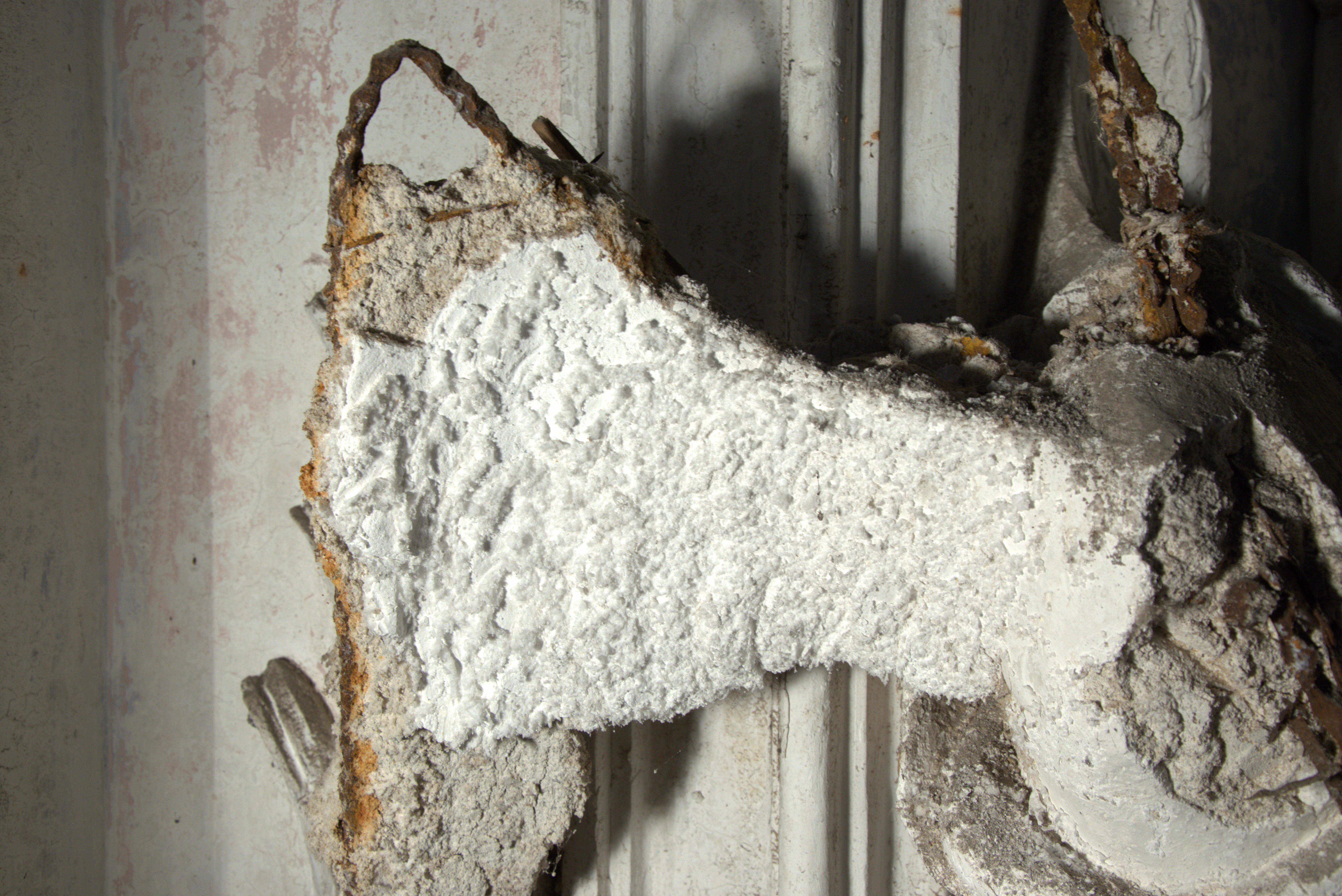 Detail of a deteriorated stucco decoration, showing exposed internal iron bars as well as coarse and finishing layers.