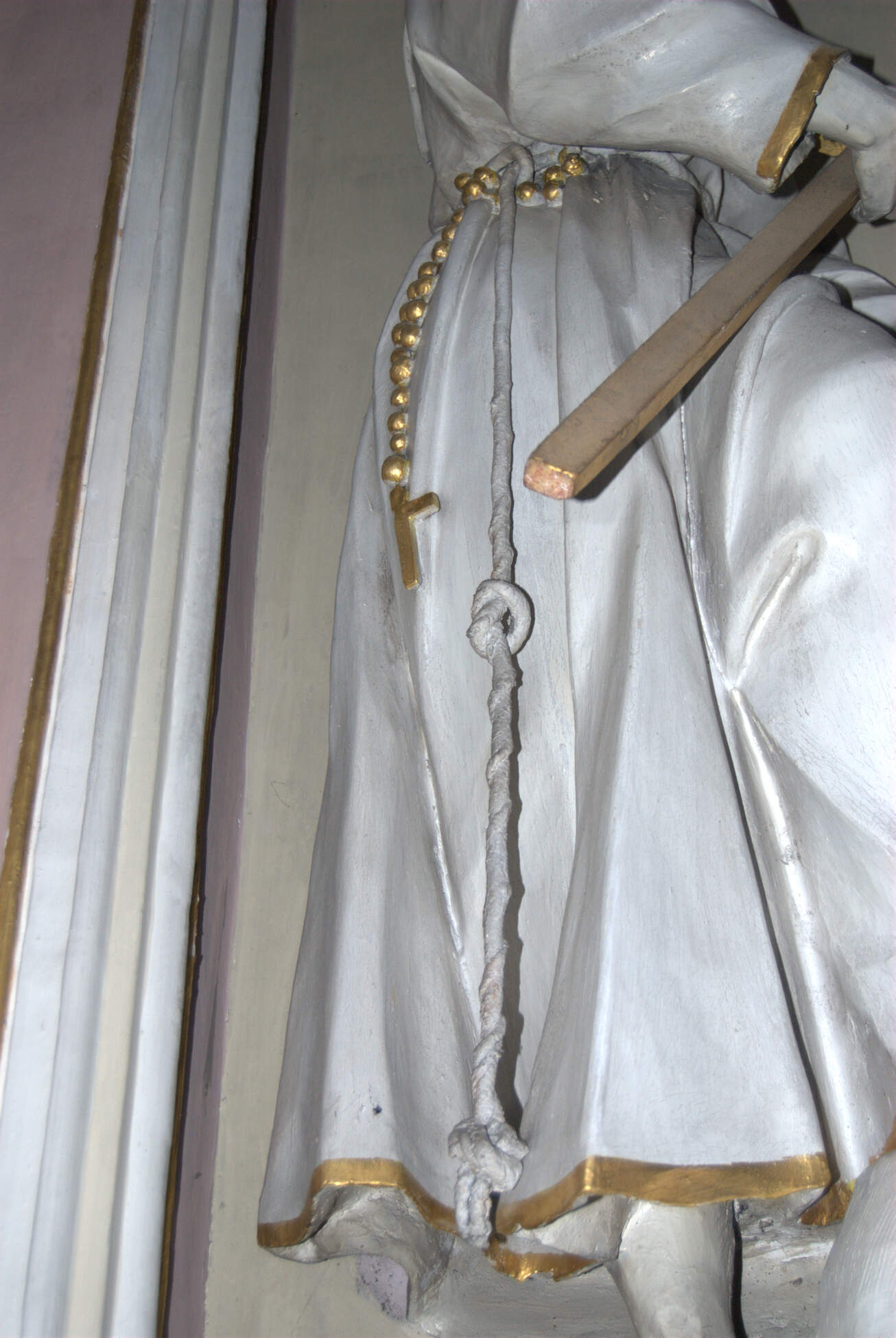 Detail of a statue of St. Peter of Alcantara, with his habit secured by a real cord painted white. The cross in his hand is made of wood and painted gold.