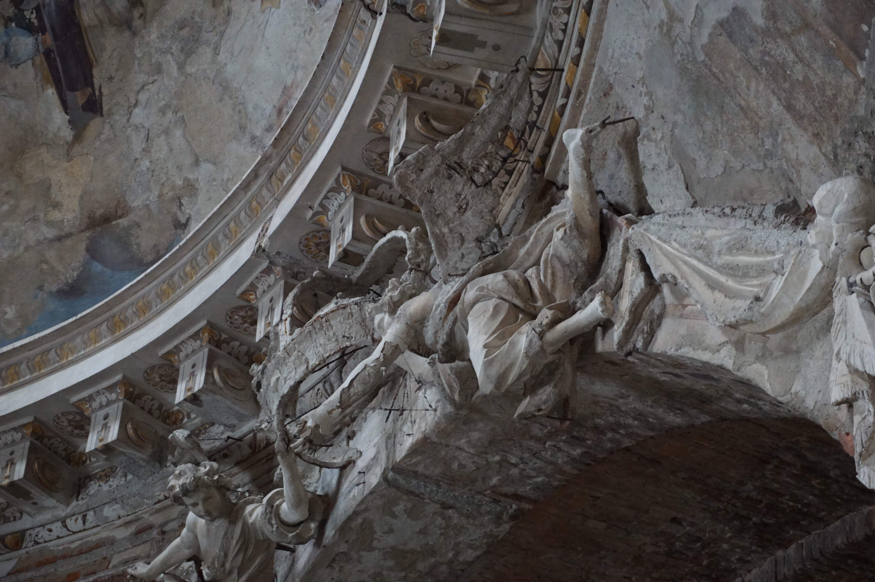 A deteriorated stucco sculpture of an angelic figure with an exposed internal structure, showing iron armatures and two layers of stucco (ground and finishing layers).