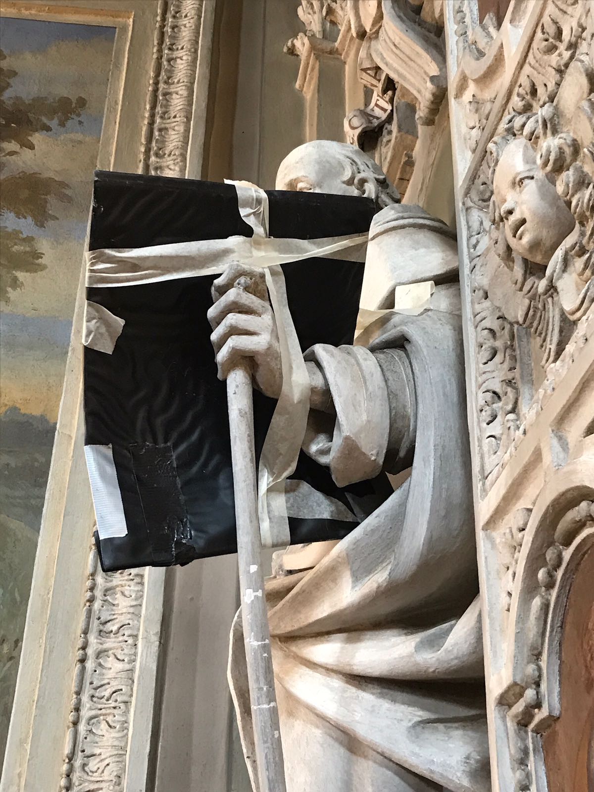 The arm of a statue prepared for an X-ray, with a black plate placed behind it to capture the image.